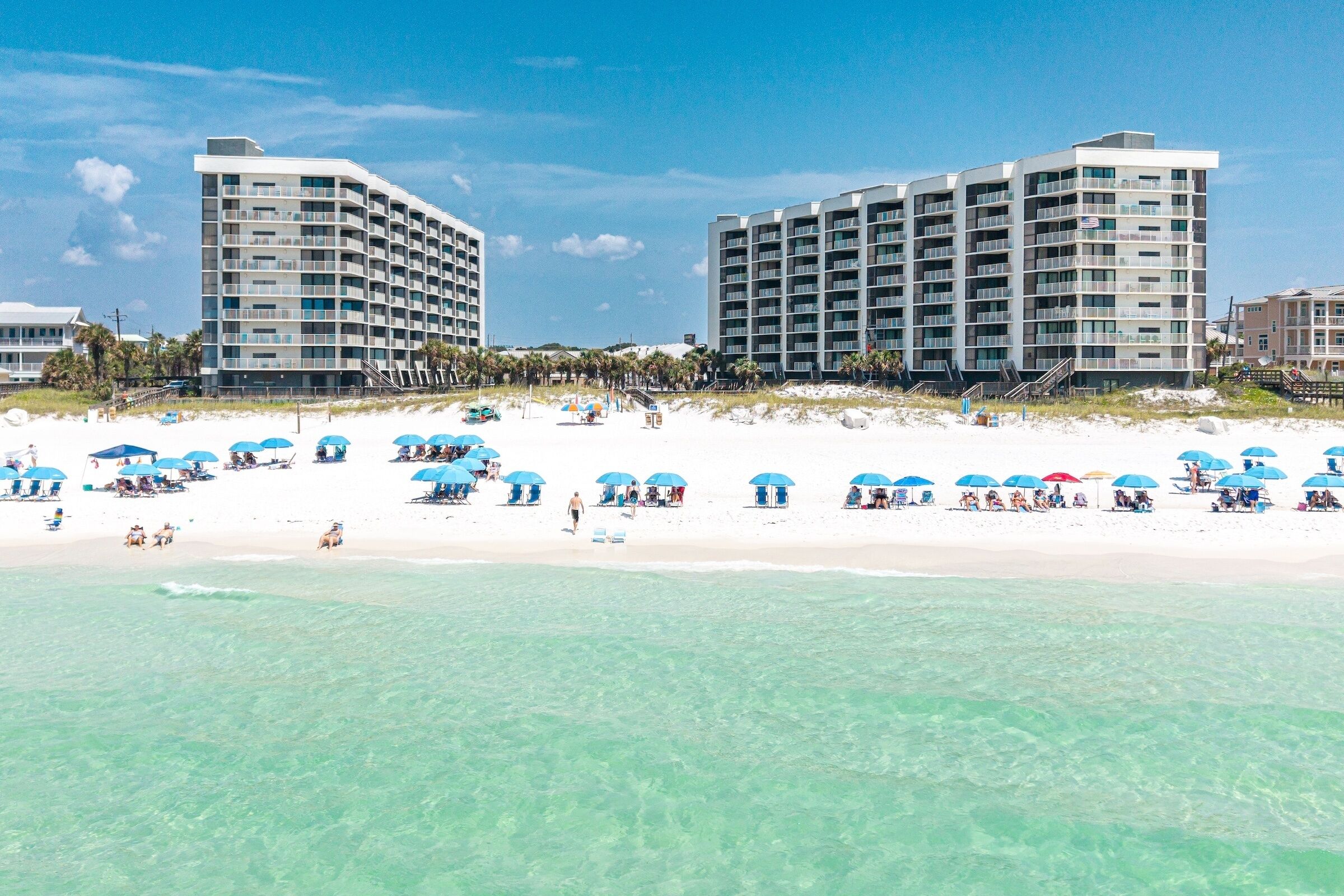 A beachfront hotel with multiple balconies, a sandy beach, and clear turquoise waters.