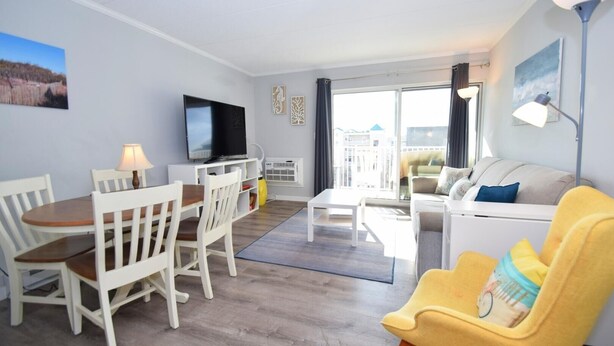 A modern living room with a dining area, a flat-screen TV, and a sofa. - Diamond Head 502 1 Bedroom Condo (Ocean City)