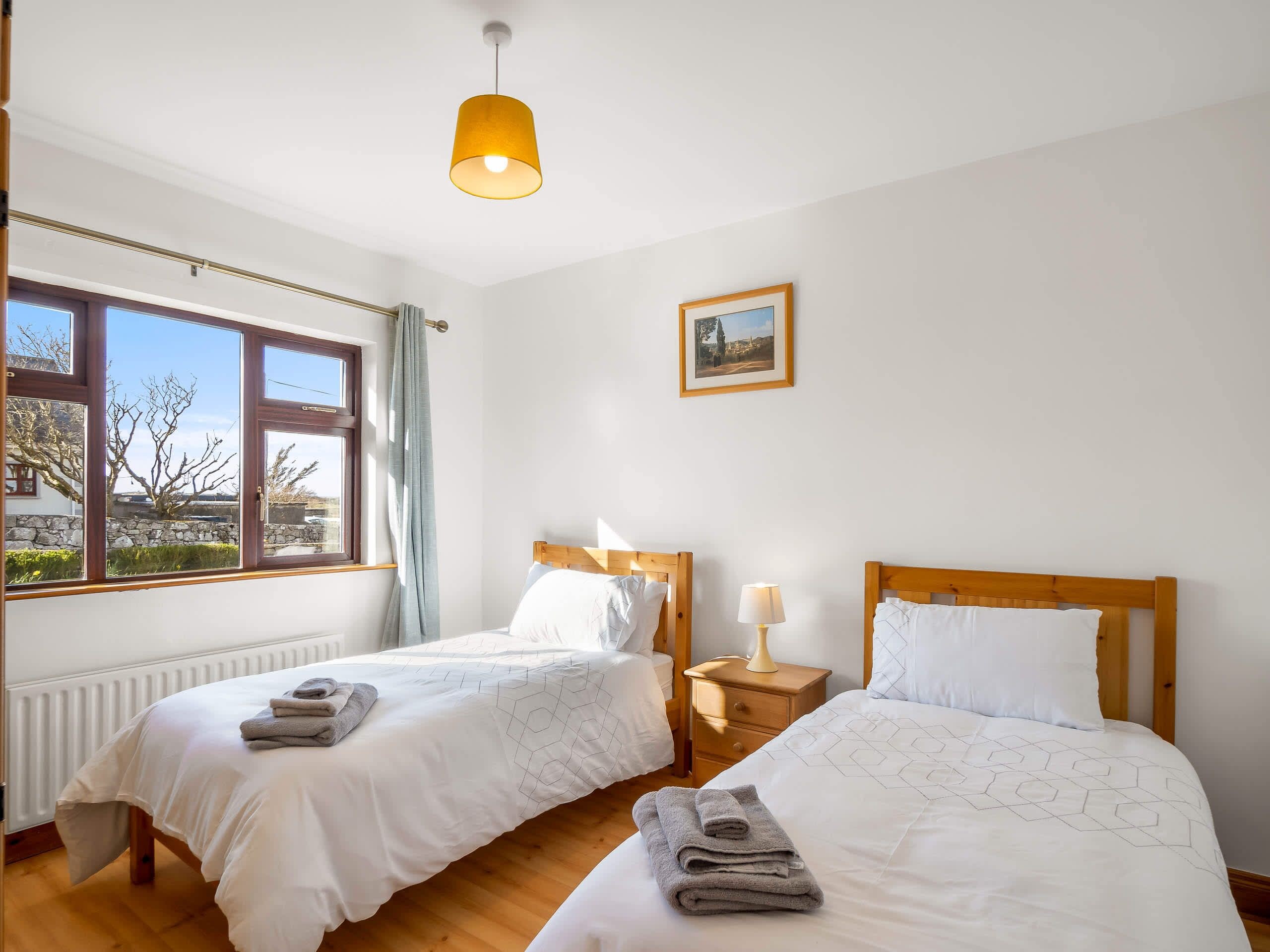 Une chambre d’hôtel avec deux lits, une fenêtre donnant sur un beau paysage, un tableau au mur et une lampe sur la table de chevet.