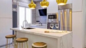 Een moderne keuken met een marmeren kookeiland, vier barkrukken, roestvrijstalen apparatuur en hanglampen.