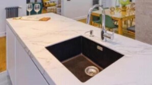 Een moderne keuken met een marmeren aanrecht, een spoelbak en gouden hanglampen.