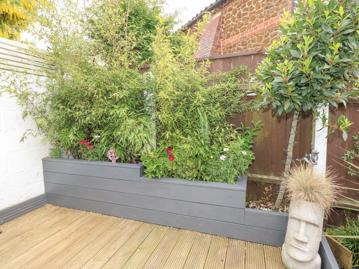 Een houten terras met een plantenbak vol verschillende planten en bloemen.