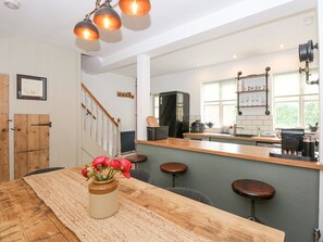 A modern kitchen with a wooden dining table, bar stools, and a vase of flowers. - Joy's Cottage (King's Lynn)