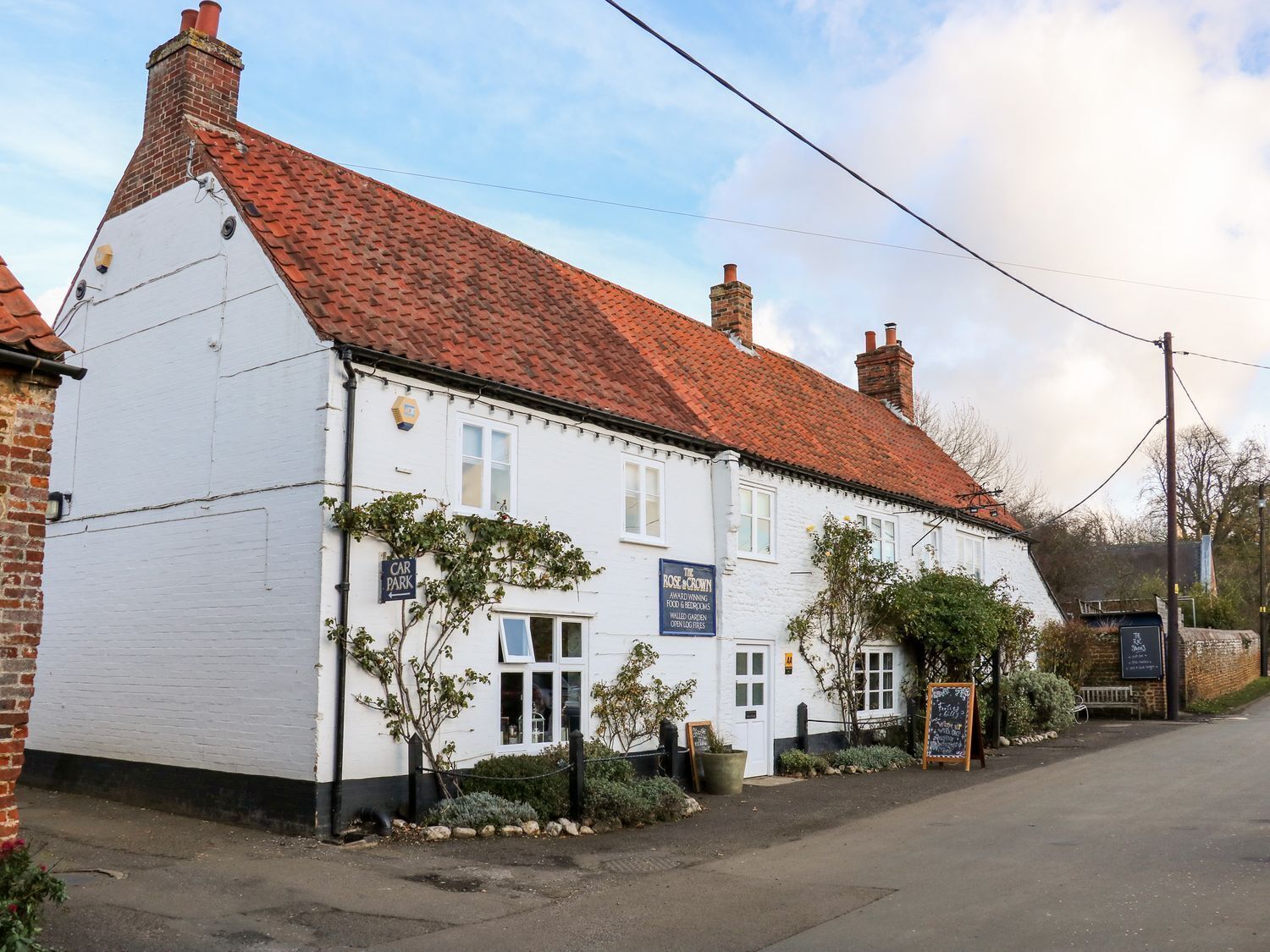 A white building with a red tiled roof, a sign for 'The Rose Inn', and a 'Car Park' sign.
