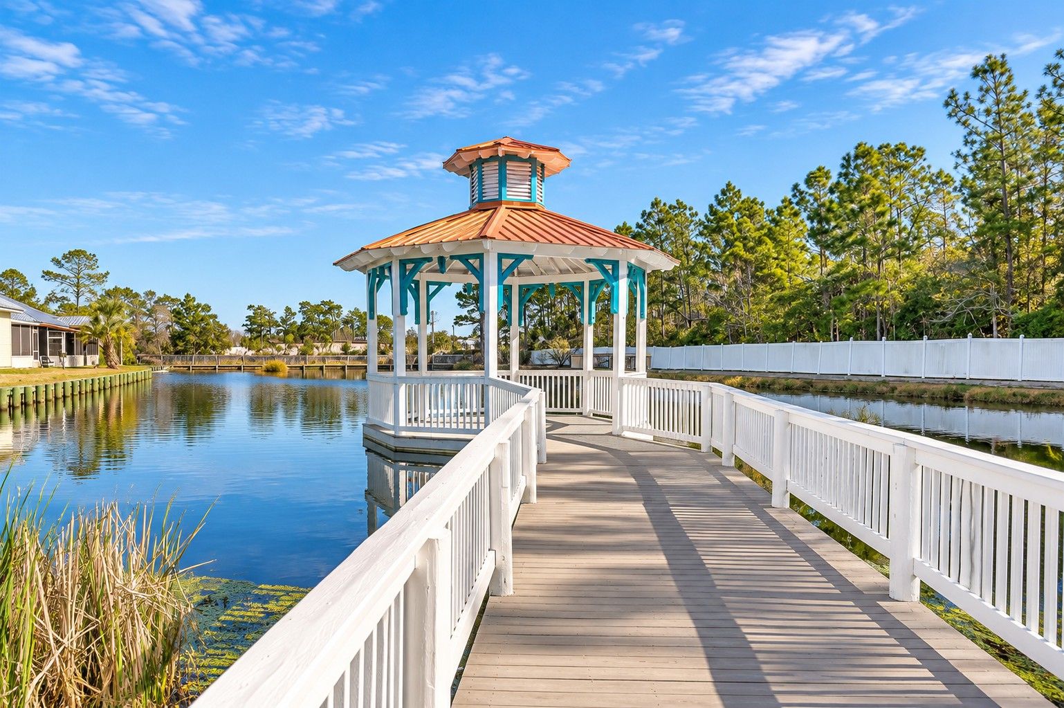A wooden boardwalk leading to a gazebo with a red roof, surrounded by water and trees.