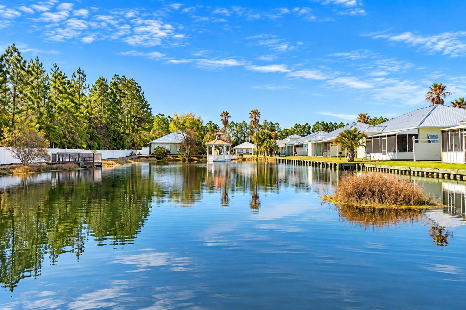 A tranquil lakeside setting with a row of cabins, a gazebo, and a clear sky.
