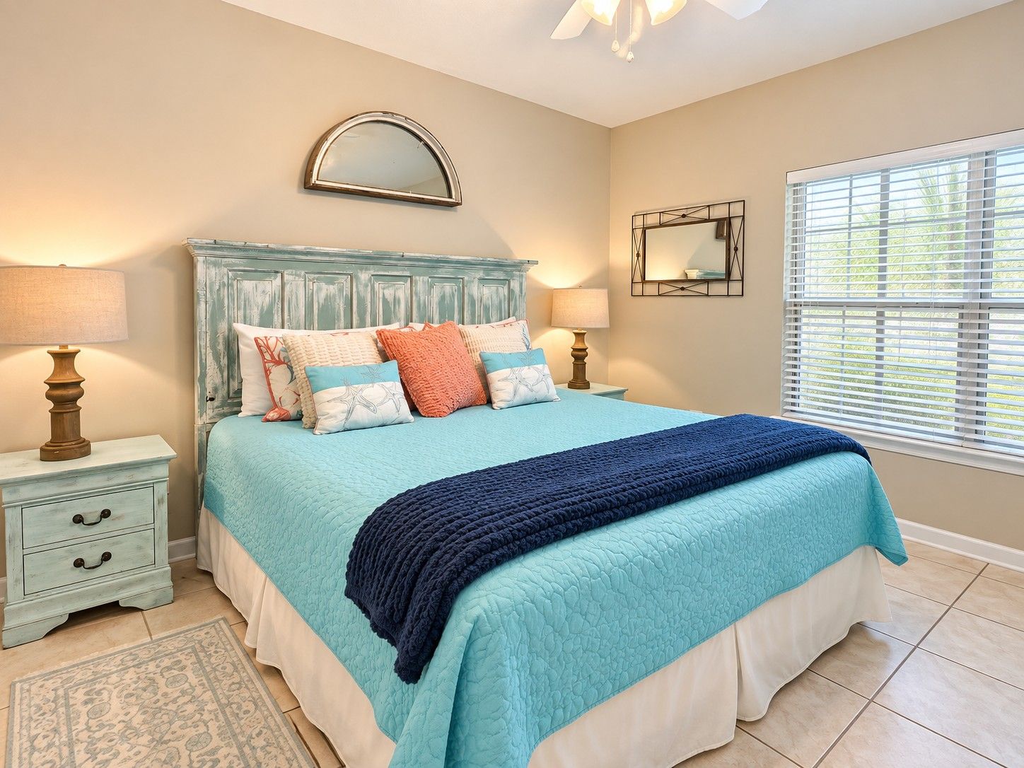 A bedroom with a bed, bedside tables, lamps, a mirror, and a window with blinds.