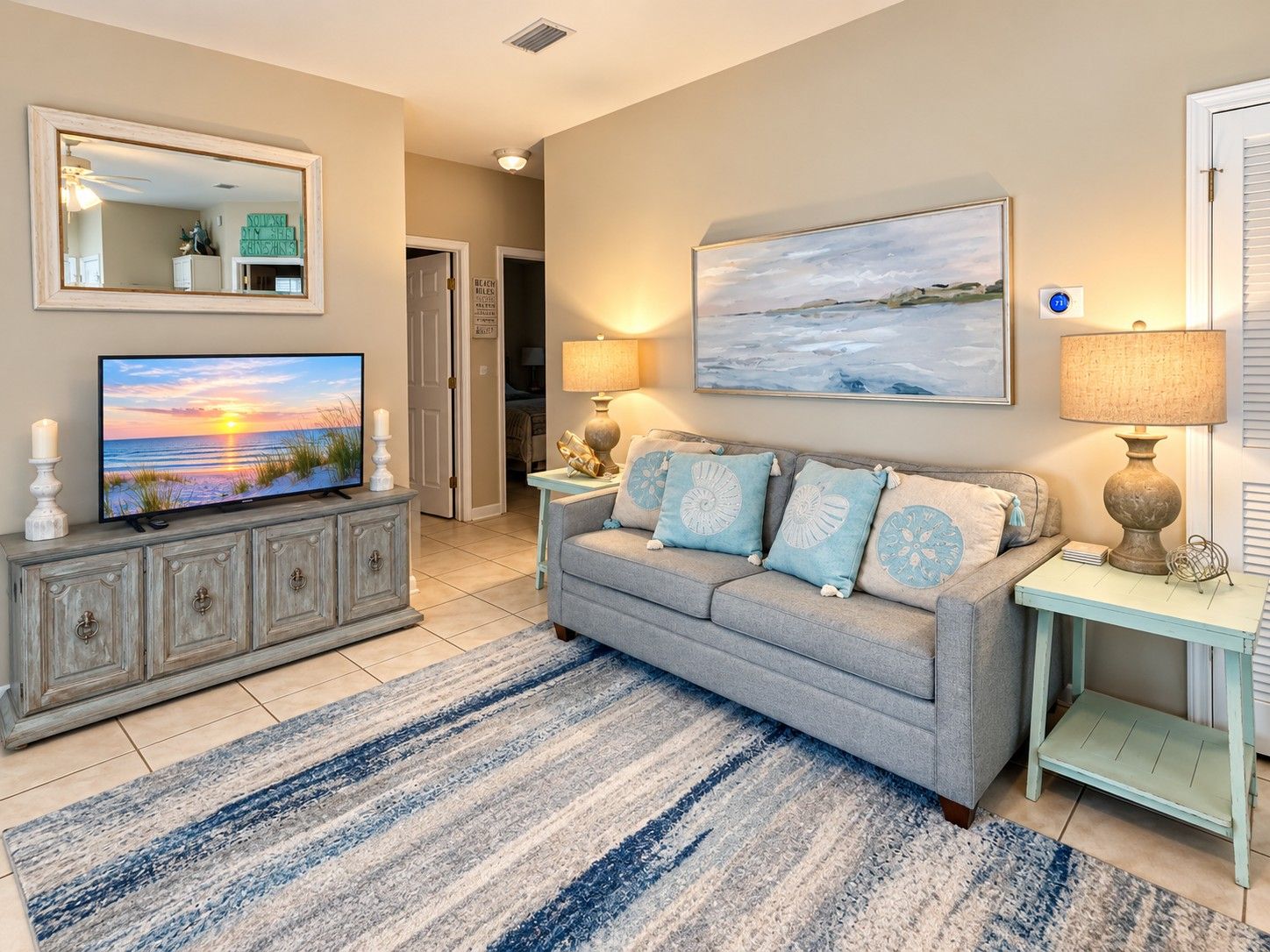 Una sala de estar con televisor, un sofá con almohadones decorativos, un cuadro y una lámpara.