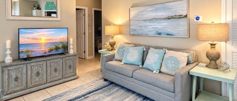Una sala de estar con televisor, un sofá con almohadones decorativos, un cuadro y una lámpara.