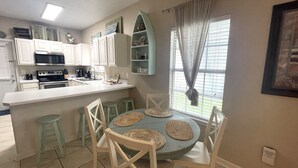 Une cuisine avec des meubles blancs, un four à micro-ondes et un évier. On y trouve également un coin repas avec une table ronde et quatre chaises.