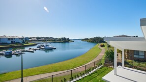 A riverside view with boats docked, a pathway, and residential buildings. - 2 Ulmarra - Spacious 4-bedroom waterfront holiday home (Harrington)