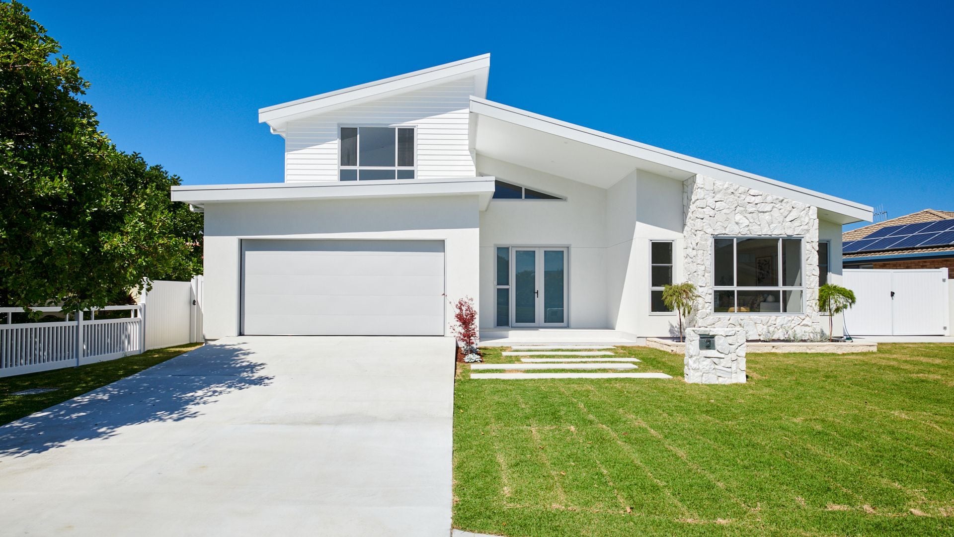 A modern two-story house with a garage, a stone accent wall, and a well-maintained lawn.