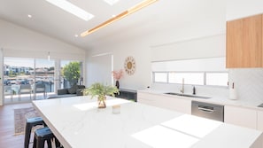 A modern kitchen with a large island, a dining area with a sofa, and a view of the outdoors. - 2 Ulmarra - Spacious 4-bedroom waterfront holiday home (Harrington)