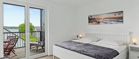 A bedroom with a bed, bedside tables, a chair, a balcony with a view, and a painting on the wall.