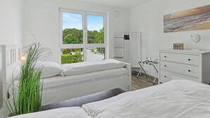 Een slaapkamer met twee bedden, een raam met uitzicht op groen, een witte dressoir en een schilderij aan de muur.