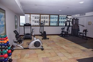 Ein Fitnessstudio mit Cardiogeräten, Kurzhanteln und einem Fenster mit Blick auf die Stadt.