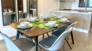 A dining table set with white plates, bowls, and wine glasses, surrounded by modern chairs. - Chic 2BR Apt 1km from Playa Bonita (Las Terrenas)