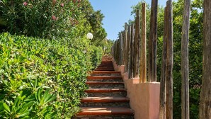 A staircase with terracotta steps, flanked by lush green foliage and wooden posts. - Pellicano by Interhome (Villasimius)