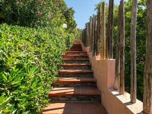 A staircase with terracotta steps, flanked by lush green foliage and wooden posts. - Pellicano by Interhome (Villasimius)