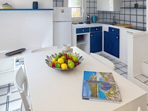 A modern kitchen with white cabinets, a blue backsplash, and a dining area with a white table. - Pellicano by Interhome (Villasimius)