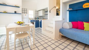 A modern kitchen with white cabinets, a dining table with chairs, and a blue sofa with colorful cushions. - Pellicano by Interhome (Villasimius)