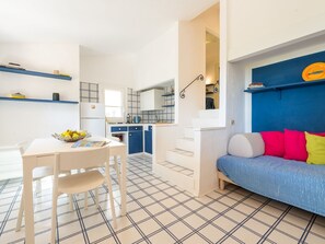 A modern kitchen with white cabinets, a dining table with chairs, and a blue sofa with colorful cushions. - Pellicano by Interhome (Villasimius)