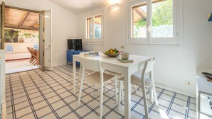 A compact kitchen with a tiled floor, a dining table with chairs, a blue cabinet, and a television. - Pellicano by Interhome (Villasimius)