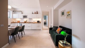 Une cuisine moderne avec des meubles blancs, un coin repas comprenant une table et des chaises, et un canapé vert agrémenté d’une lampe.