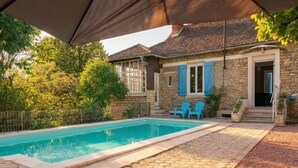 Una piscina con sedie blu, un edificio in pietra con persiane blu e un'area patio coperta.