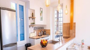 Una cucina moderna con isola centrale, forno integrato, frigorifero e finestra con persiane blu.