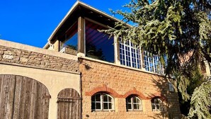 Un edificio in pietra con un'ampia porta in legno, finestre ad arco e un albero sullo sfondo.