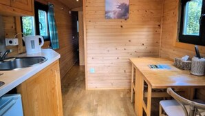 Une petite cabane en bois comprenant un coin cuisine, une table à manger et des chaises.