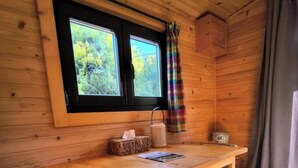 L’intérieur d’un chalet en bois comprend une table à manger, deux chaises, une fenêtre avec un rideau et une petite table sur laquelle se trouvent une boîte de mouchoirs et une bougie.