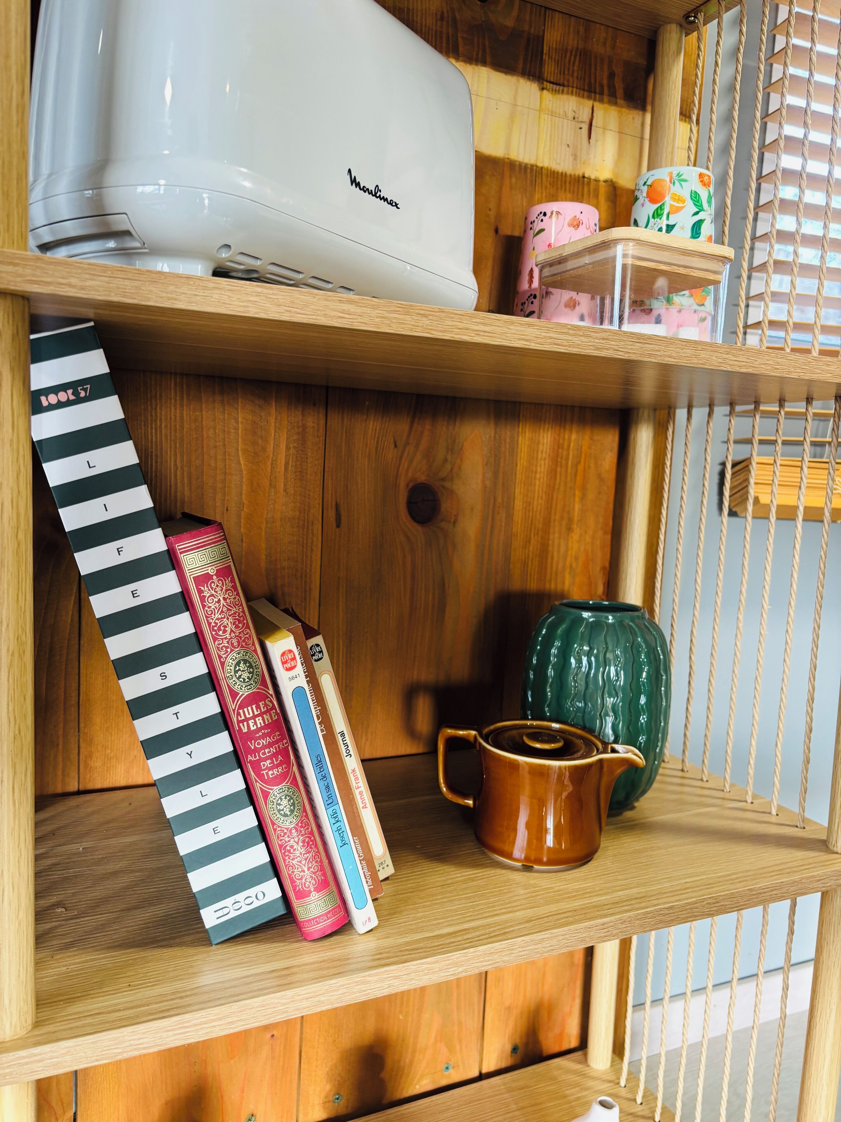 Une étagère en bois sur laquelle on aperçoit un appareil électroménager blanc, des livres, une tasse et des objets décoratifs.