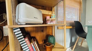 Une étagère en bois sur laquelle se trouvent un appareil électroménager blanc, des livres, un vase vert et une chaise noire.