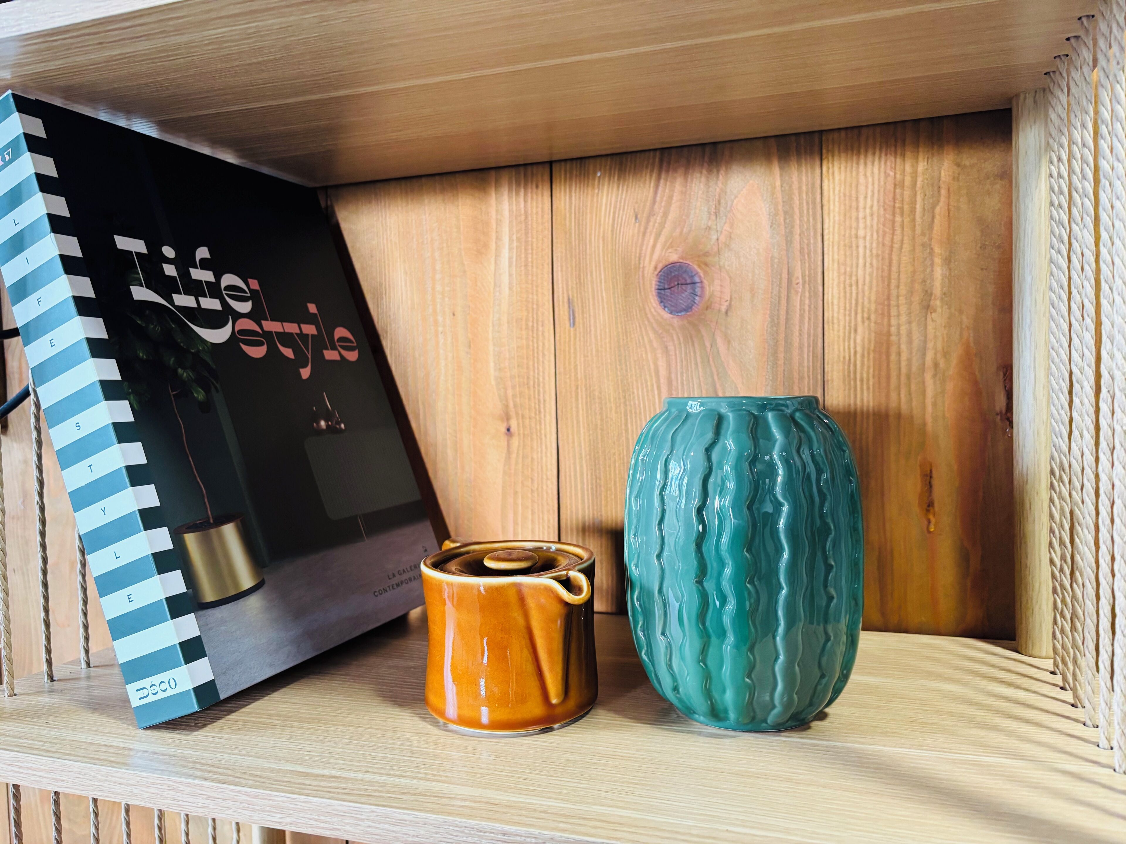Une étagère avec un livre à spirale, une tasse en céramique et un vase à motifs.