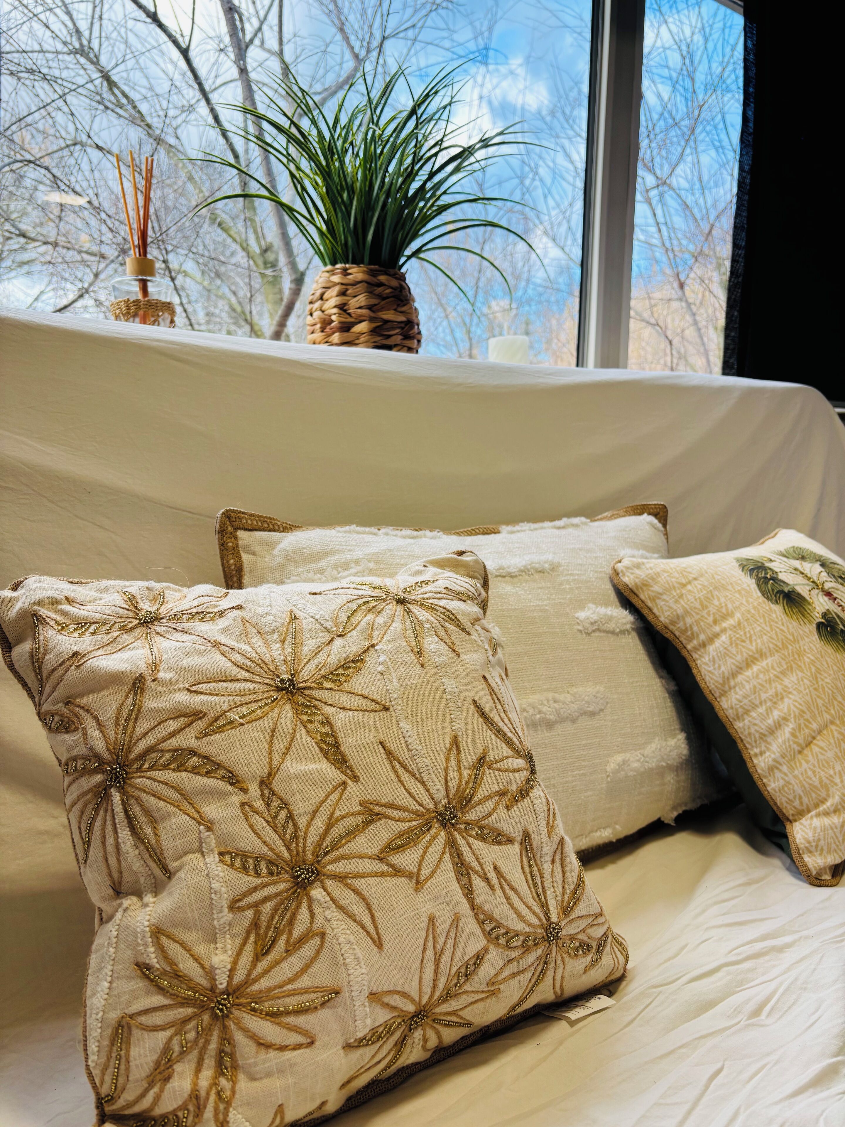 Ein Bett mit beigefarbener Bettwäsche und dekorativen Kissen mit Blumenstickerei.