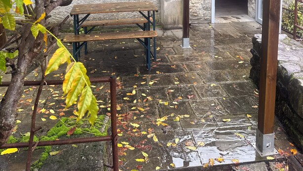 A stone patio with a wooden bench and a metal table, surrounded by trees with green and yellow leaves. - Le Case di Rosie (Fivizzano)