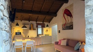 A cozy interior with a dining area, kitchen, and a living room with a sofa and a painting of a flamingo. - Le Case di Rosie (Fivizzano)