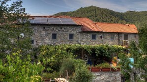 A stone building with a red-tiled roof, solar panels, and a garden with climbing plants. - Le Case di Rosie (Fivizzano)
