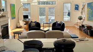 A modern kitchen with a gas stove, pots, and a kettle. There is a dining area with a sofa and chairs, a fireplace, and artwork on the walls. - August or weekly rental bike to beach, walk to tennis! (Westerly)