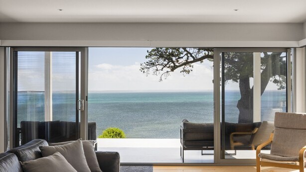 Una sala de estar moderna con un amplio ventanal corredero que da a un balcón con vistas al mar.
