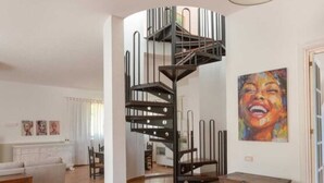 A spacious living area with a spiral staircase, a large painting, and a dining area in the background. - Villa Sole (Lecce)
