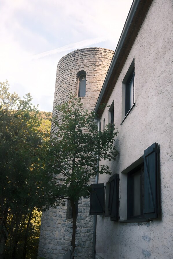 A stone tower attached to a building with windows and shutters.