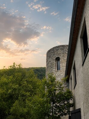 Une tour de pierre dotée d’une fenêtre, entourée d’arbres, et un bâtiment dont le mur présente une texture particulière.