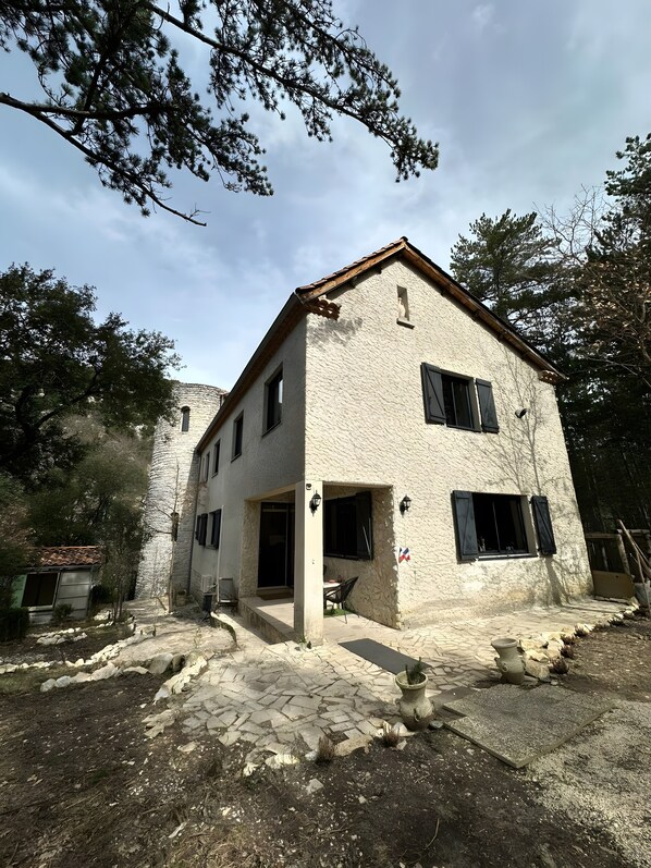 A two-story building with a stone facade, a tiled roof, and a small porch area.
