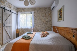 Ein Schlafzimmer mit Steinwand, hölzernem Bettgestell, einem Fenster mit Vorhängen und einer Klimaanlage.