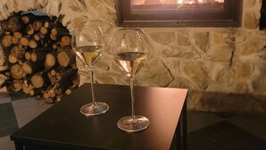 A stone fireplace with a fire, two wine glasses on a table, and a stack of firewood. - Bed & Breakfast “La Lisière” with Mountain View, Wi-Fi and Air Conditioning (Brantes)