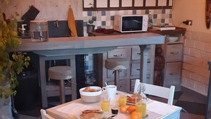 A kitchen with a dining table, chairs, a microwave, and a clock on the wall. - Bed & Breakfast “La Lisière” with Mountain View, Wi-Fi and Air Conditioning (Brantes)