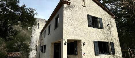 Un edificio de dos pisos con fachada de piedra, techo de tejas y un pequeño porche.